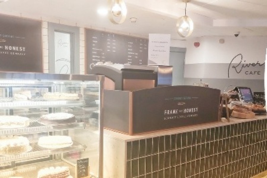 The bakery counter inside The River Cafe, with a glass cake display, tiled counter front and pendant lighting